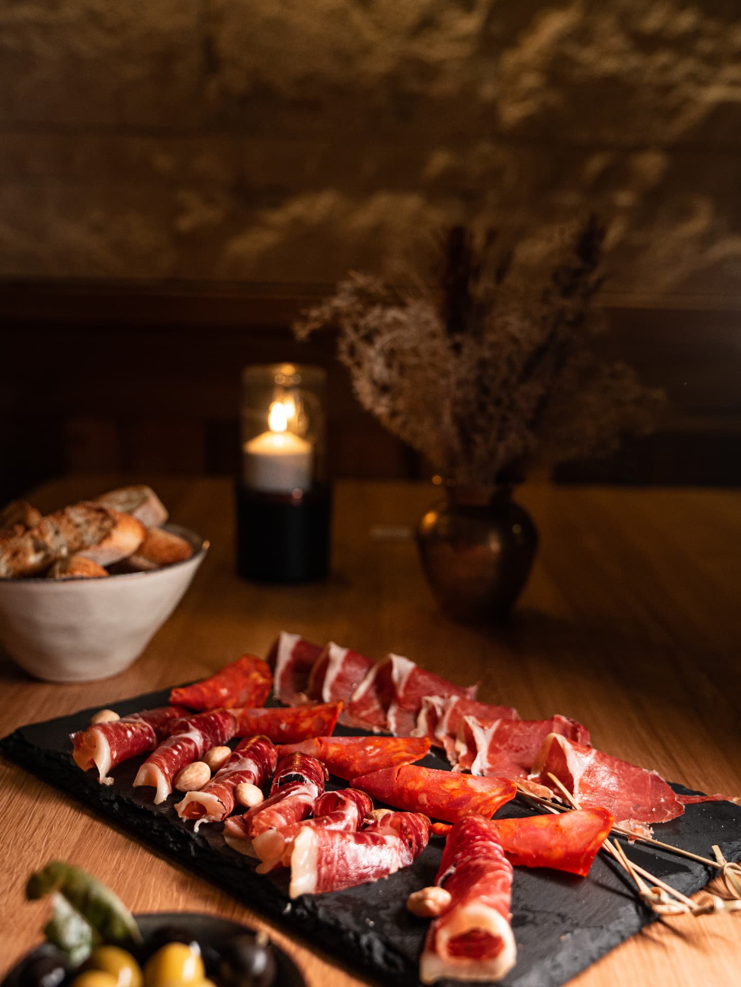 Schinken- und Chorizoplatte auf dunkler Schieferplatte mit Brot und Kerzenlicht