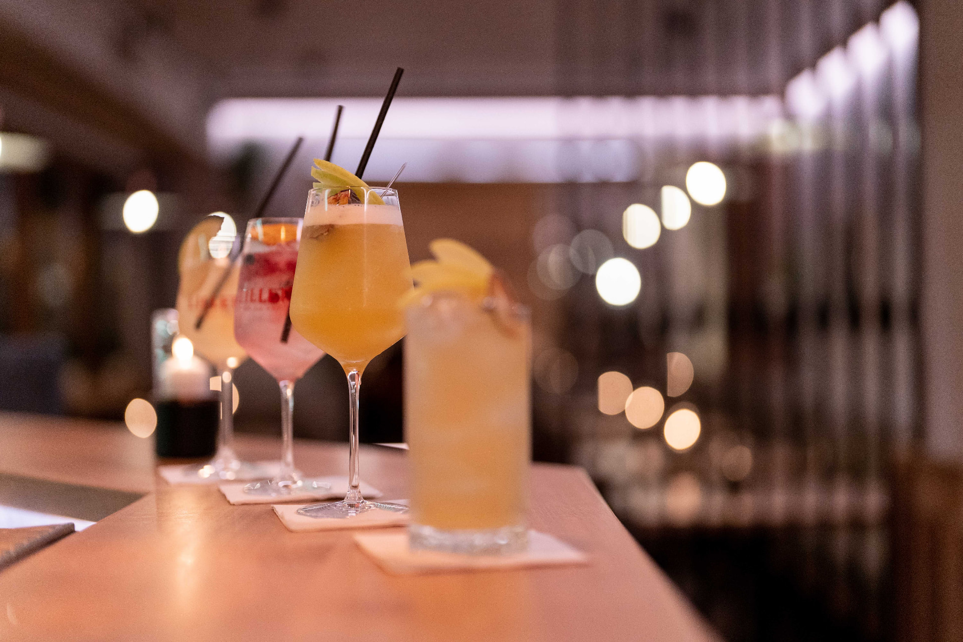 Drei Cocktails auf der Bartheke mit Bokeh-Lichtern im Hintergrund